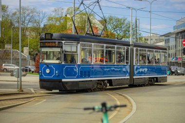 Mavi ve beyaz bir klasik tramvay Tallinn 'de virajlı bir pistte ilerliyor. Kadriorg 'a giden tramvay, parlak ve bulutlu bir gökyüzü altında bir şehir kavşağından geçiyor..