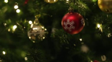 Beyaz kar tanesi desenli kırmızı bir Noel mücevheri yeşil bir köknar dalına asılır. Yumuşak bir şekilde peri ışıklarıyla aydınlatılır. Arka planda kremalı bokeh, sakin ve şenlikli bir bayram havası yaratır..