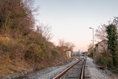 Altın saat buzet tren istasyonu, taş binalar ve kavisli rayların yanında antika bir platform. Sıcak gün batımı ışığı yakınlardaki evleri ve kayalık tepeleri yıkıyor, sakin, kırsal bir Istrian manzarası yaratıyor..