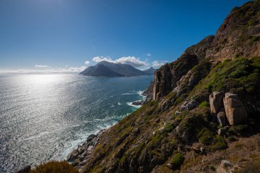 Bu görüntü Hout Bay 'in ve Sentinel dağ zirvesinin manzaralı Chapmans Peak Drive' dan ikonik görüntüsünü gösteriyor. Derin turkuaz Atlantik suları engebeli, kayalık bir kıyı şeridiyle buluşur..