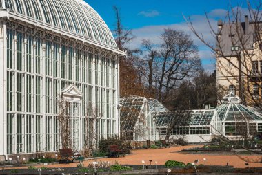Helsinki Üniversitesi Botanik Bahçesi 'nin zarif, beyaz Palm House' u mavi gökyüzüne karşı parlak bir şekilde duruyor. Karmaşık 1889 cam mimarisi çakıl yollarına ve baharda uyanan bahçe yataklarına bakıyor..