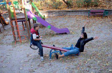 Mutlu anne ve oğul büyük yeşil bir salıncakta birlikte geziyorlar, güneşli bir gün ve açık havada ailecek vakit geçiriyorlar.