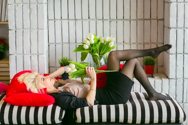 Beautiful blonde girl on the couch with a bouquet of flowers . t — Stock Photo, Image