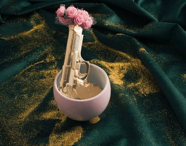 Golden gun in pink vase with pink flower on green fabric with golden glitter.