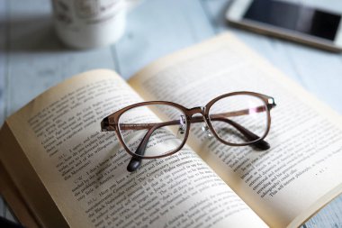 Karton kapaklı kitap ve gözlük, kahve içerken okumak, dinlenme zamanı.