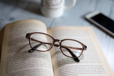 Karton kapaklı kitap ve gözlük, kahve içerken okumak, dinlenme zamanı.