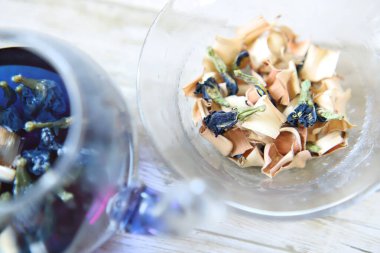 Bright blue color butterfly pea flower herb tea in a glass tea pot and dried tea on a plate