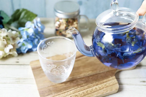 Poring bright blue butterfly pea flower herb tea to a glass from glass tea pot