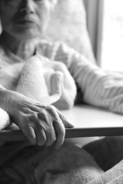 Bunamış yaşlı bir kadın hemşire yatağında dinlenirken bir masaya tutunuyor.