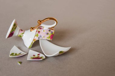 Çiçek desenli kırık bir pembe porselen bardak ve basit gri arka planda bir plaka. Tabağında çiçek deseni olan pembe seramik çay fincanı parçalanmış. Kırık çay fincanı pembe ve gri arka planda.. 