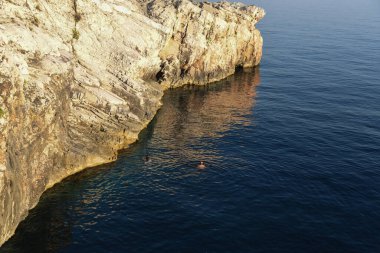 Man swimming in the beautiful deep blue sea next to the rocky cliff