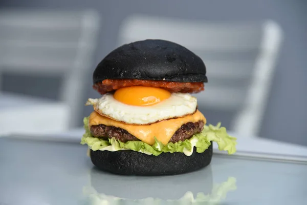 Tasty black bread burger with leaking egg, meat, salad, red sauce and cheddar isolated on simple bright background