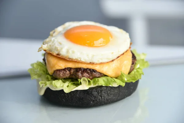 Tasty black bread burger with leaking egg, meat, salad, red sauce and cheddar isolated on simple bright background
