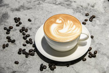 Kahve fincanı dolusu kremalı kahve mermer masanın üzerinde kahve taneleri süslemesi.