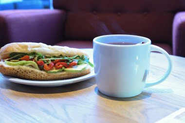 Çay dolu çay ve çay poşeti. Arkaplanda ahşap masa ve sandviç