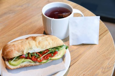 Çay dolu çay ve çay poşeti. Arkaplanda ahşap masa ve sandviç