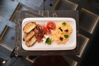  Lezzetli kızarmış yumurta, jambon ve siyah tabakta domuz pastırması. Bıçak ve çatal, tabağın yanındaki peçeteye.