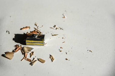 Beyaz masadaki paslı kalem kesicisi ve kalemden kesilmiş tahta parçaları. güneş ışığı