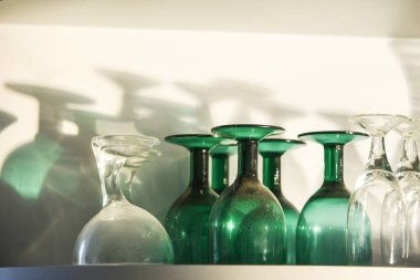 Boş bardaklar baş aşağı, gölgeler ve güneş ışığı raflarda.