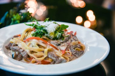 Beyaz tabakta süslemeli İtalyan makarnası. Arka planda zeytinyağı