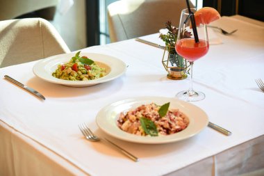 Restoranda beyaz masa örtüsü üzerinde iki renkli makarna menüsü. Dekorasyon ve içecek masada.