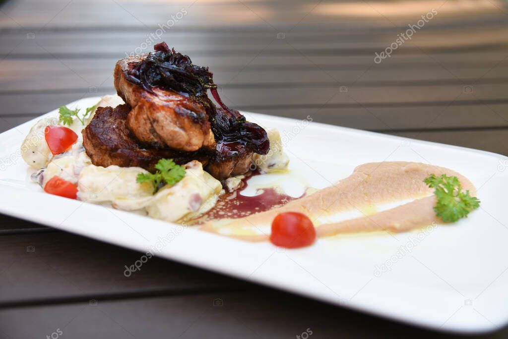 Big peace of meat on white plate with colorful decoration. Tomato and parsley with apple puree. 