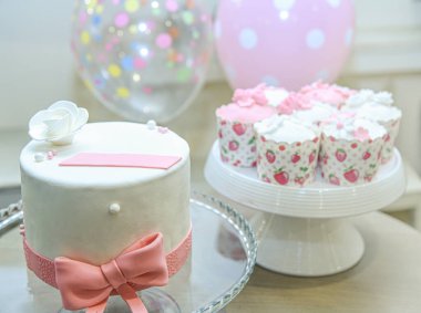 Kremalı ve şekerli güzel bir pasta ve arka planda balonlar. Dekoratif bardaklarda çörekler. Kurdeleli geleneksel pasta.. 