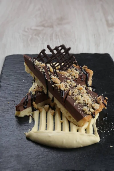 Chocolate tart cake on black marble plate in restaurant. Decoration from chocolate peaces with almond and peanuts.