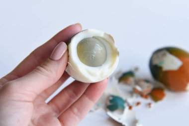 Haşlanmış yumurtanın yarısını tutan kadın eli. Tarafsız, beyaz ve kahverengi arka planda renkli Paskalya yumurtaları. Sanatsal boyanmış ve tasarlanmış yumurtalar. Yumurtanın etrafındaki yumurta parçaları. Boş kopyalama alanı