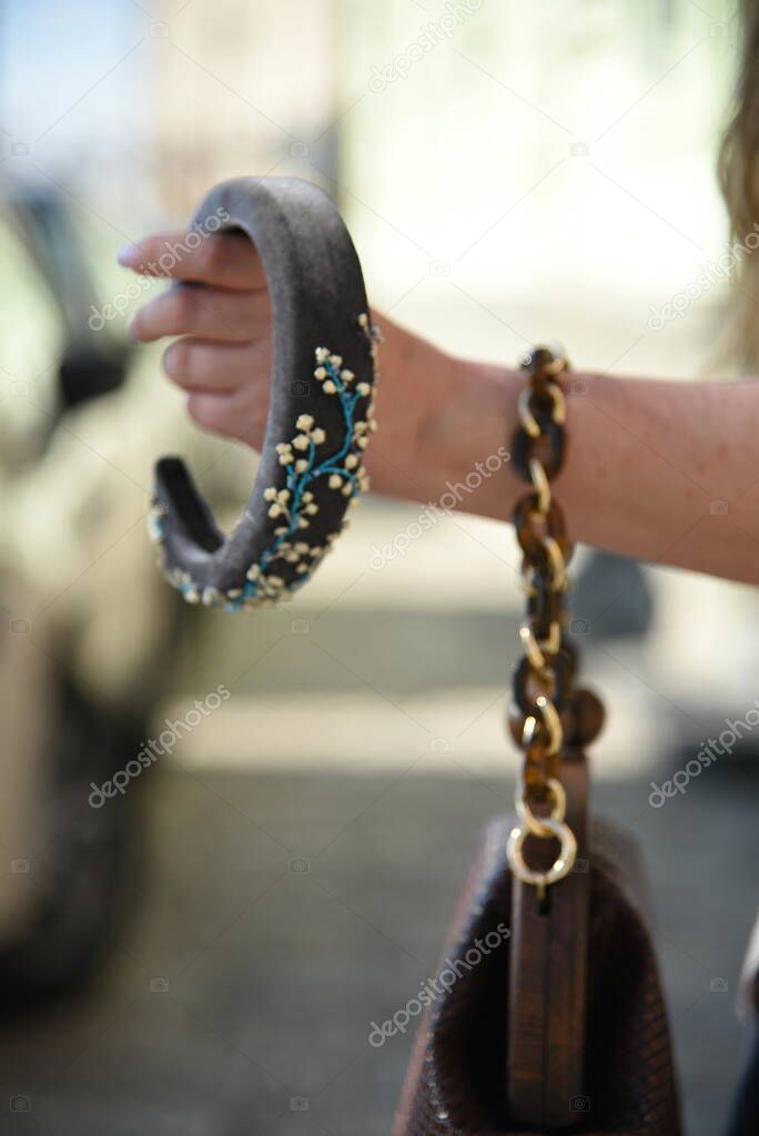 Female model with long hair holding hand bag and hairband in hand and walking on the street close up purse and hand. Empty copy space