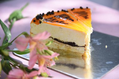 Taze portakal meyvesi ve çikolatalı kremalı lezzetli turuncu pasta. Tarafsız bir arkaplan ve bulanık çiçekler. Fındık ve krema süslemeli lezzetli çikolatalı pasta. Kremalı pasta ve çikolata süslemesi. Dekoratif tabak