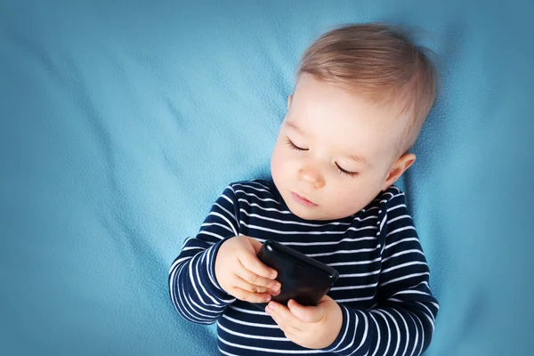 Маленький хлопчик на синьому ковдрі з мобільним телефоном — стокове фото