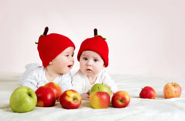 Dwa cute dzieci leżące w kapeluszach na miękki koc z jabłkami — Zdjęcie stockowe