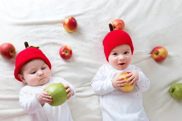 Dwa cute dzieci leżące w kapeluszach na miękki koc z jabłkami — Zdjęcie stockowe