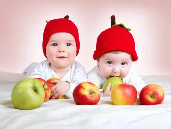 Dwa cute dzieci leżące w kapeluszach na miękki koc z jabłkami — Zdjęcie stockowe