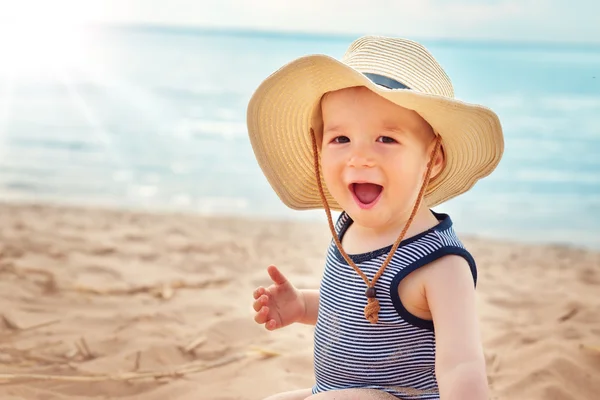 Mały chłopiec siedzi na plaży w Kapelusz Słomkowy — Zdjęcie stockowe