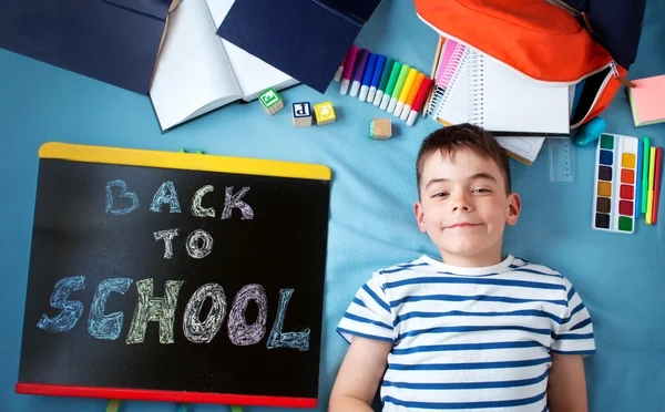 Enfant couché sur une couverture bleue avec tableau noir et accessoires scolaires — Photo