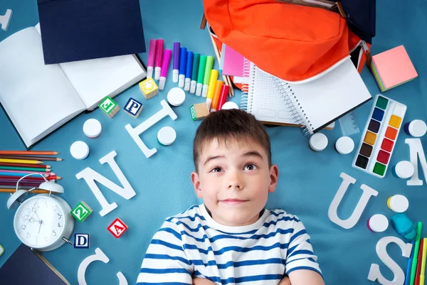 Enfant couché sur une couverture bleue avec accessoires scolaires — Photo