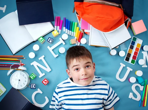 Enfant couché sur une couverture bleue avec accessoires scolaires — Photo