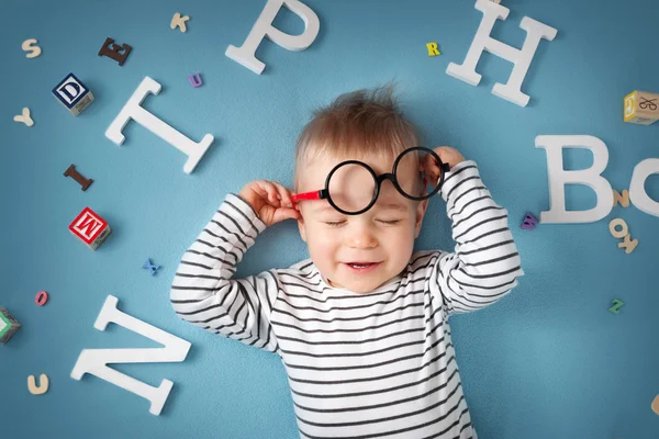 Niño de un año acostado con gafas y letras —  Fotos de Stock