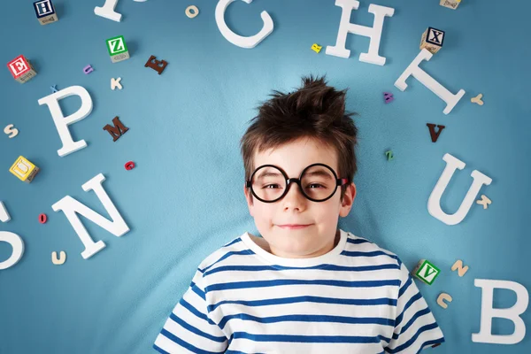 Niño de siete años acostado con gafas y letras —  Fotos de Stock