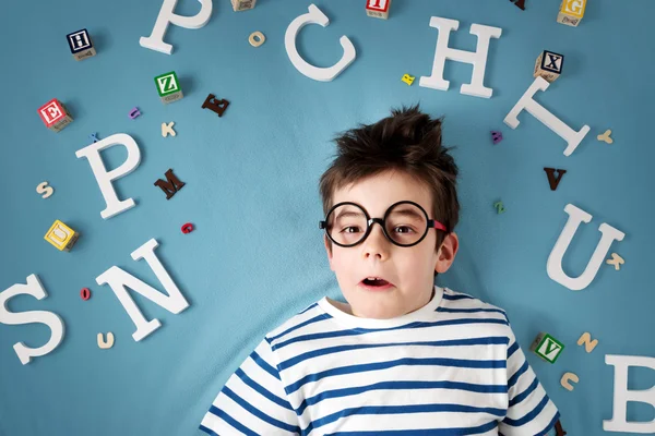 Criança de sete anos deitada com óculos e letras — Fotografia de Stock