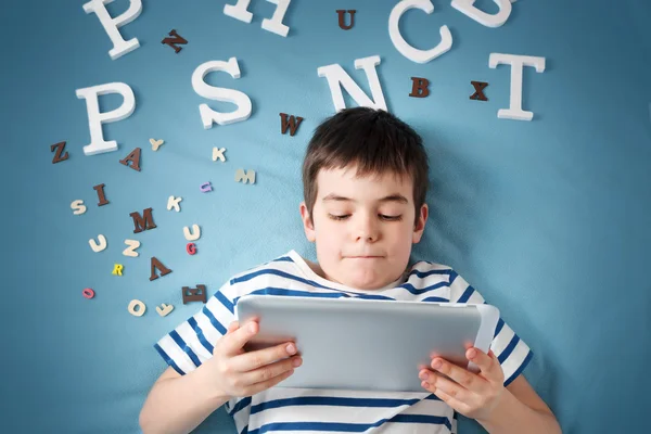 Enfant de sept ans couché avec une tablette et des lettres — Photo