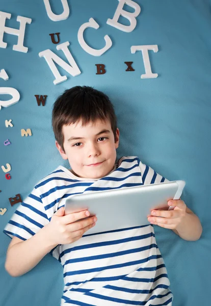 Enfant de sept ans couché avec une tablette et des lettres — Photo