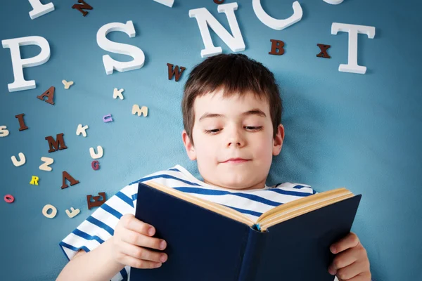 Сім років дитина лежить з книгою і літерами — стокове фото
