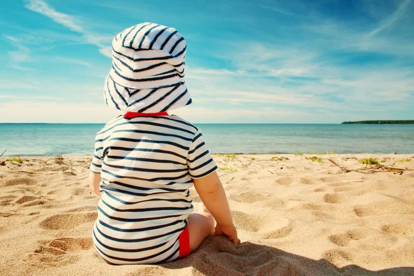 Liten pojke sitter på stranden på sommardagen — Stockfoto