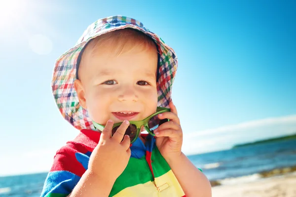 Kleine jongen glimlachend op het strand in hoed met zonnebril — Stockfoto