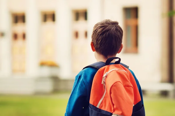 Pojke med ryggsäck infront av en skolbyggnad — Stockfoto