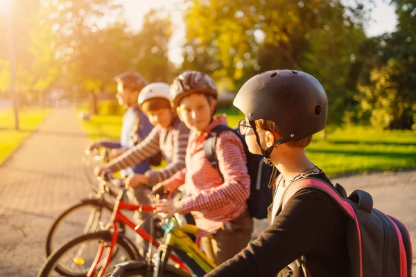 Niños con mochilas en bicicleta en el parque cerca de la escuela —  Fotos de Stock