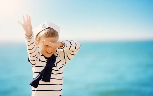 Söt pojke i sjömanshatt står på stranden av havet — Stockfoto